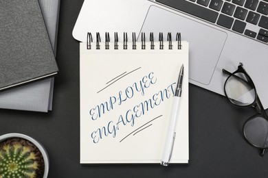 Image of Employee engagement. Words in notebook, pen and laptop on black table, top view