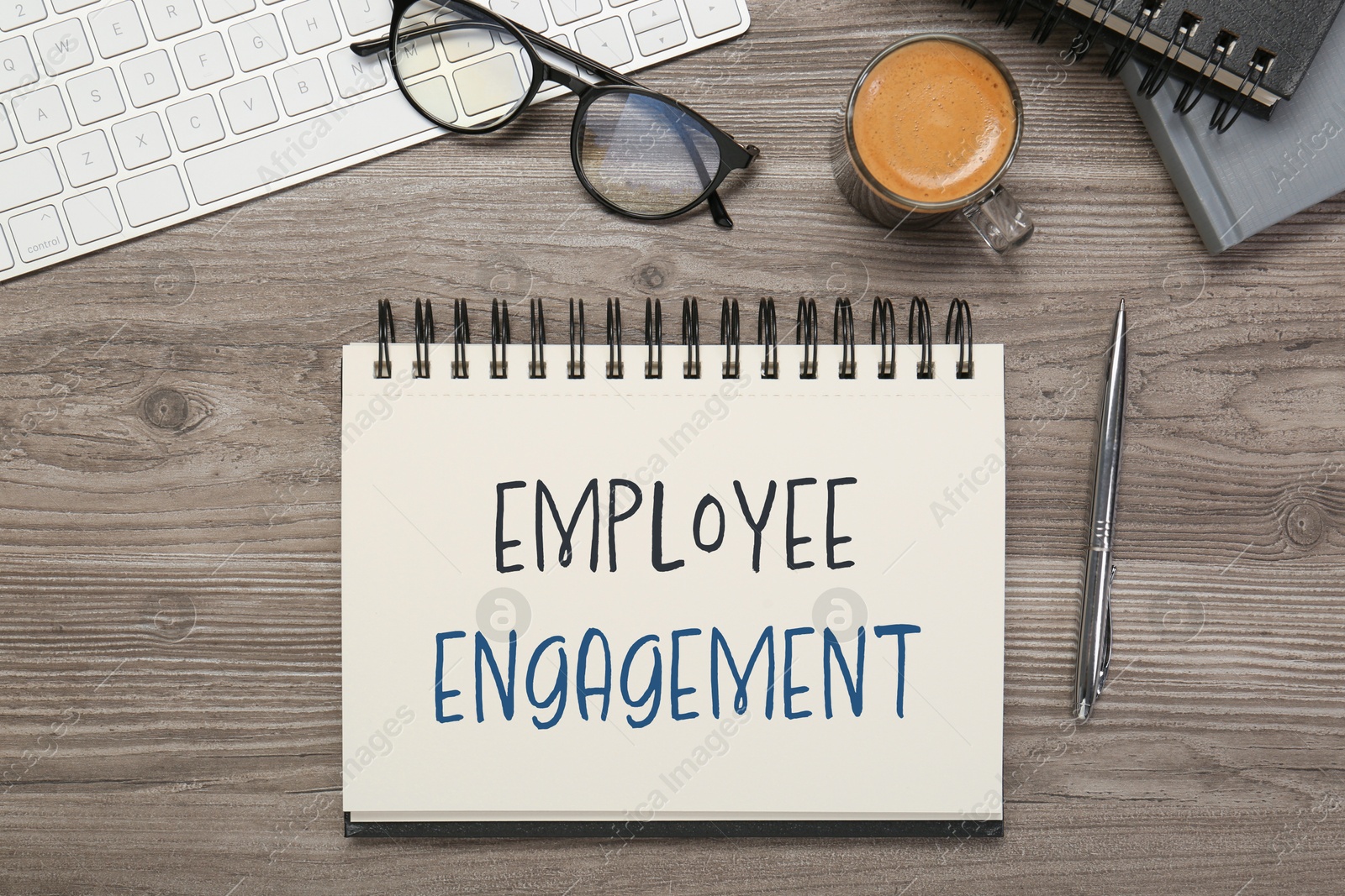 Employee engagement. Words in notebook, pen and computer keyboard on wooden table, top view Image of Employee engagement. Words in notebook, pen and computer keyboard on wooden table, top view