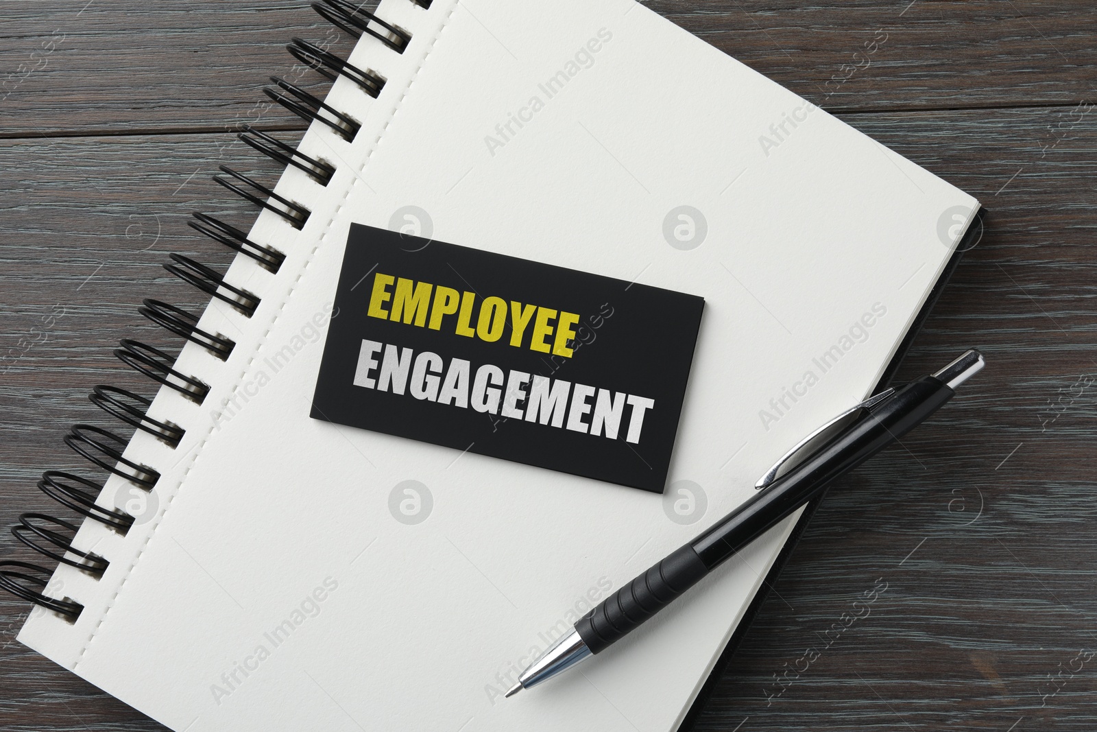 Image of Business card with words Employee Engagement, notebook and pen on wooden table, top view