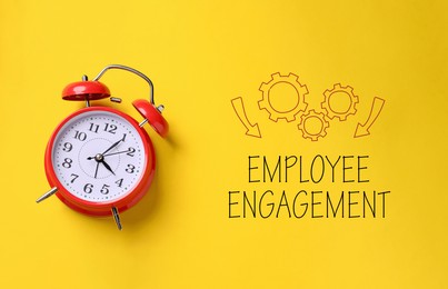 Image of Employee engagement. Red alarm clock and words on yellow background, top view