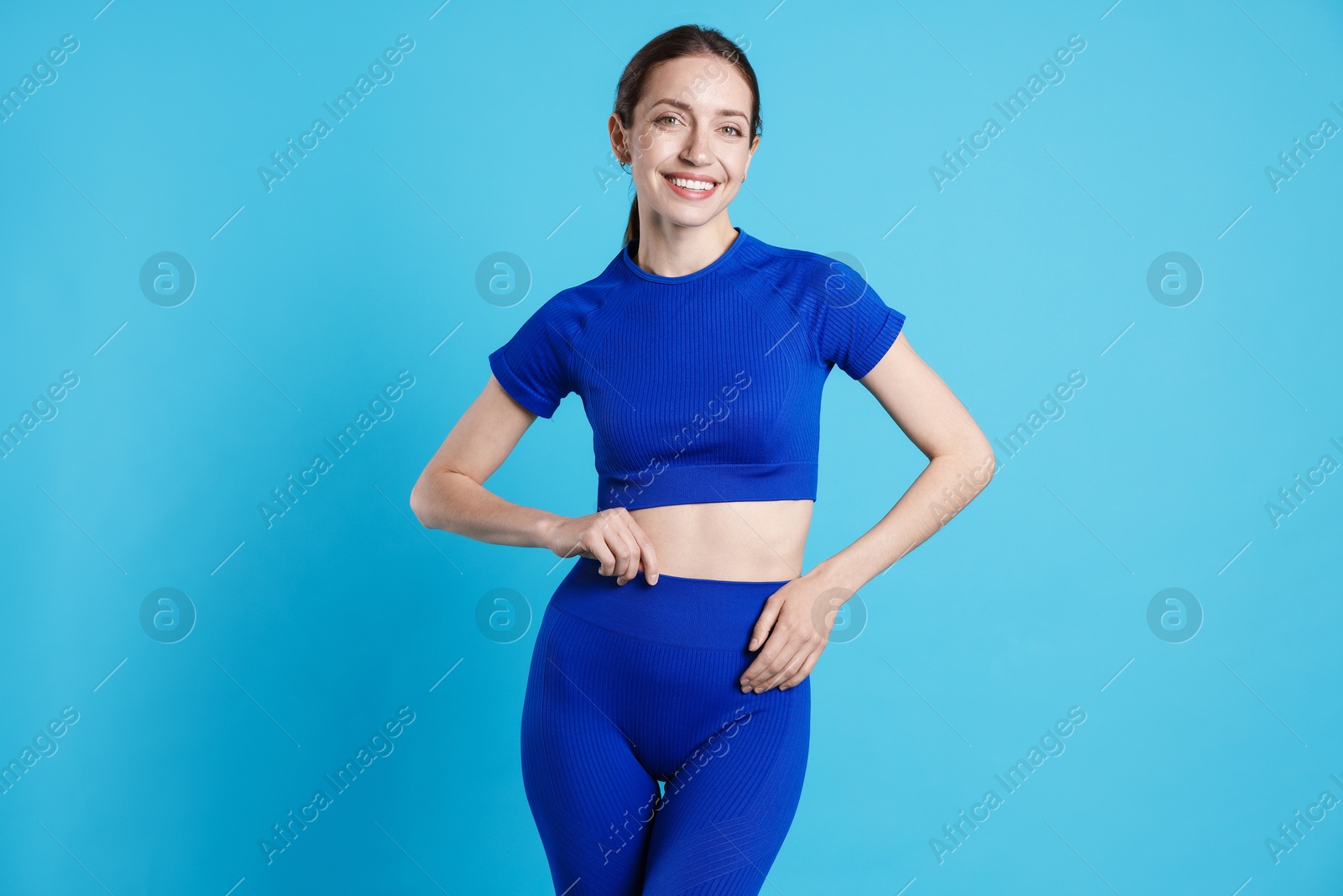 Beautiful woman with flat belly on light blue background Photo of Beautiful woman with flat belly on light blue background