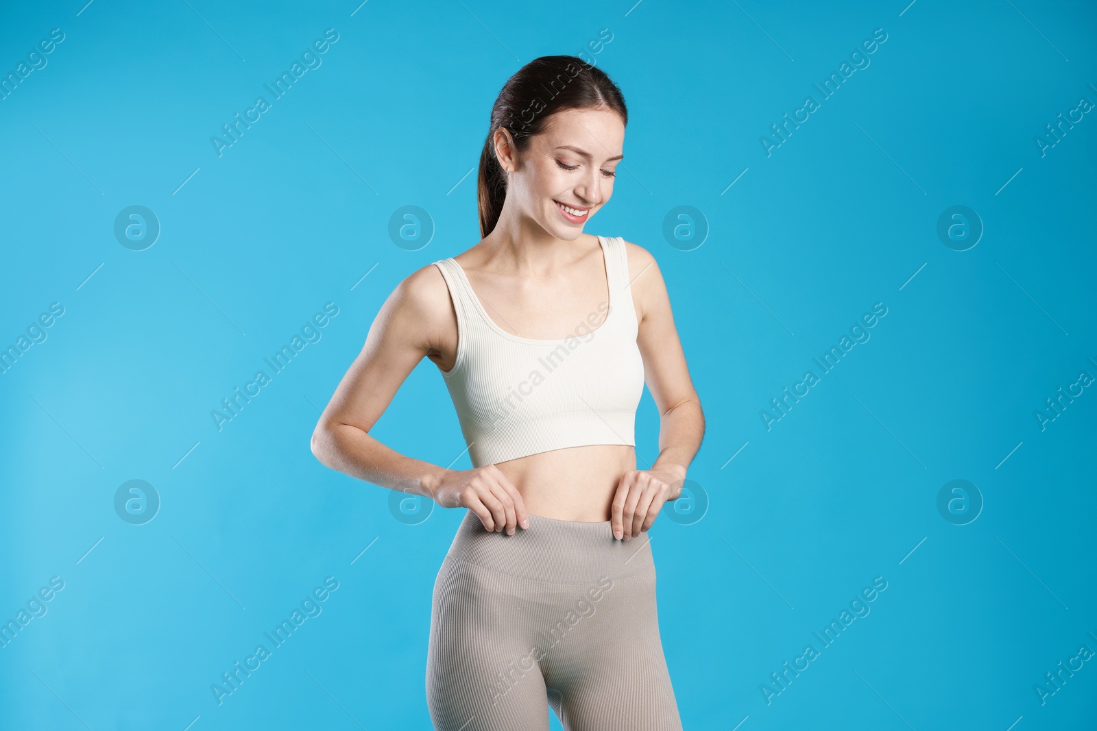 Beautiful woman with flat belly on light blue background Photo of Beautiful woman with flat belly on light blue background