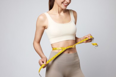 Photo of Woman measuring her belly with tape on gray background, closeup