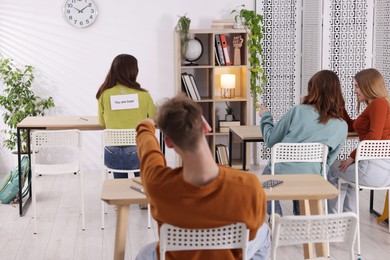 Photo of Schoolmates bullying teenage girl with sign You Loser on her back at school