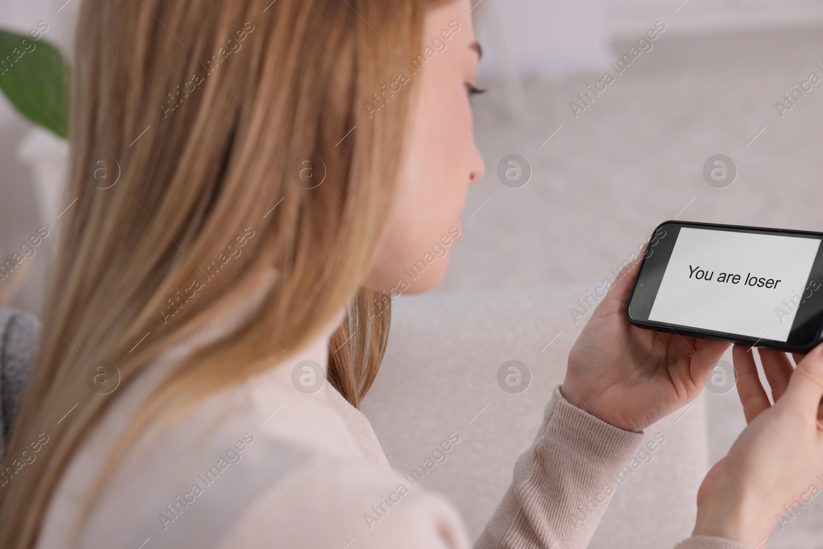 Cyber bullying. Upset teenage girl looking at smartphone with text You Loser at home, closeup Photo of Cyber bullying. Upset teenage girl looking at smartphone with text You Loser at home, closeup
