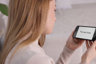 Photo of Cyber bullying. Upset teenage girl looking at smartphone with text You Loser at home, closeup