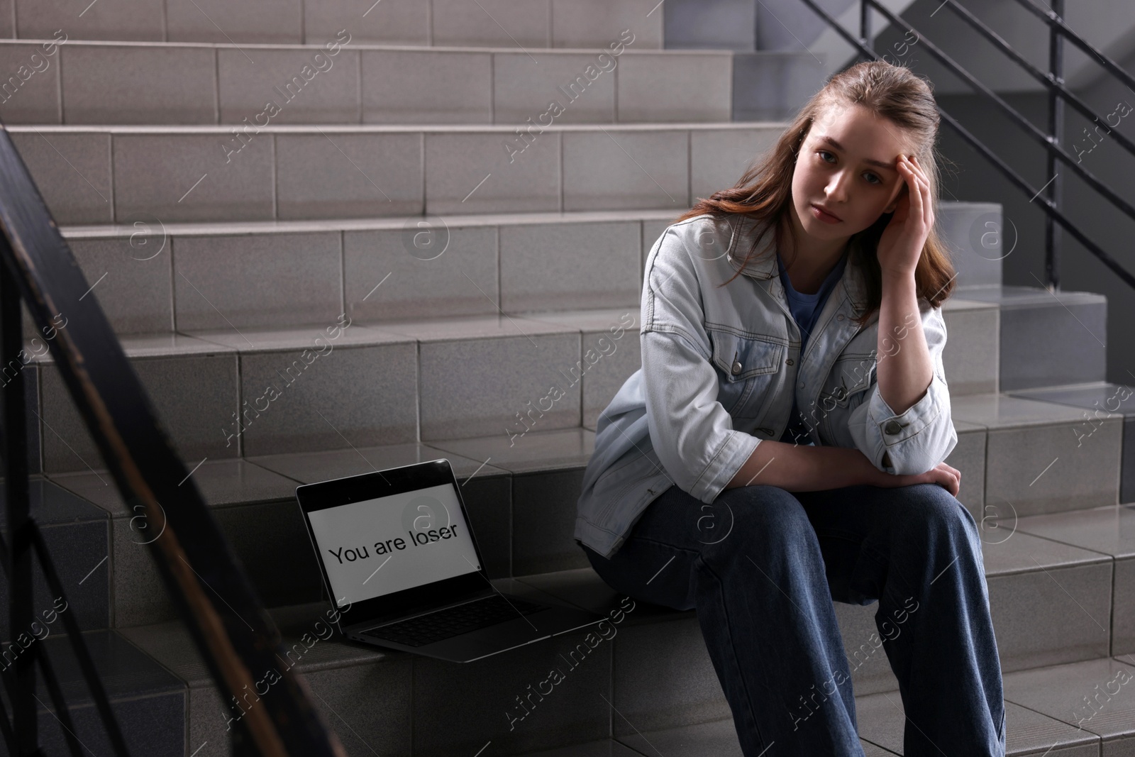 Cyber bullying. Upset teenage girl and laptop with text You Loser on stairs indoors Photo of Cyber bullying. Upset teenage girl and laptop with text You Loser on stairs indoors