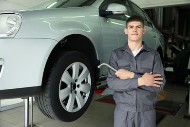 Photo of Professional mechanic with wrench near lifted car in garage