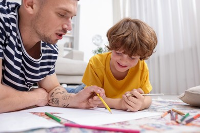 Photo of Father teaching his son to draw on floor at home