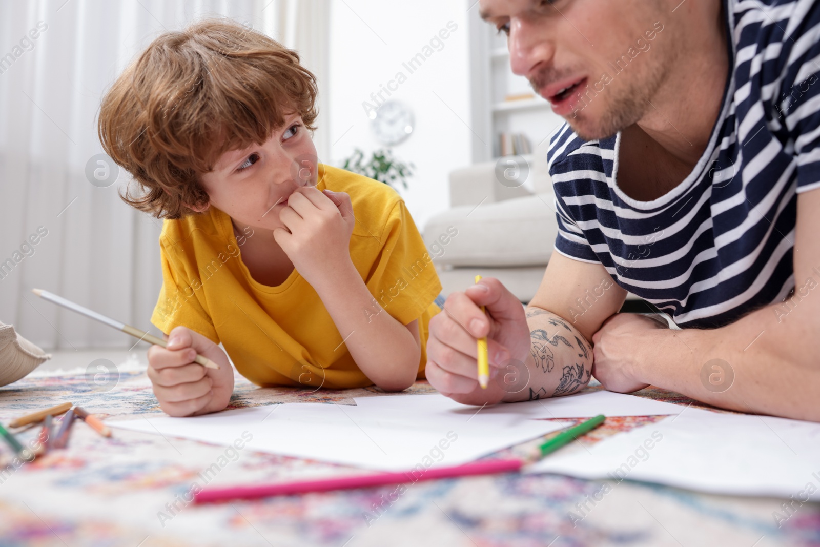 Photo of Father teaching his son to draw on floor at home, closeup