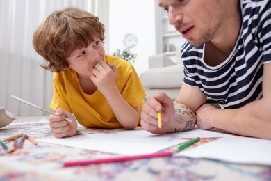 Photo of Father teaching his son to draw on floor at home, closeup