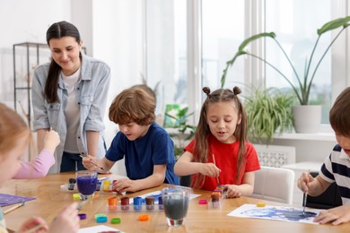 Photo of Woman teaching kids to draw at painting lesson indoors