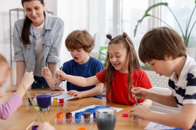 Photo of Woman teaching kids to draw at painting lesson indoors