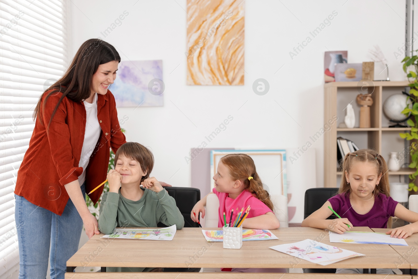 Woman teaching kids to draw at painting lesson indoors Photo of Woman teaching kids to draw at painting lesson indoors