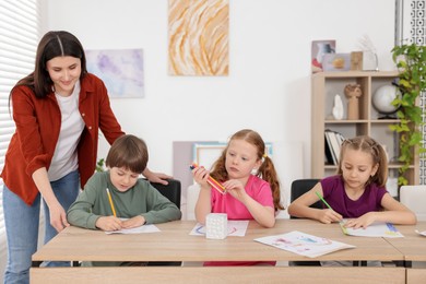 Photo of Woman teaching kids to draw at painting lesson indoors