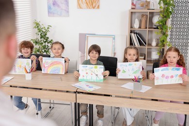 Photo of Kids showing their drawings to teacher at painting lesson indoors, selective focus