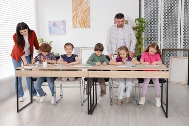 Photo of Kids with teachers at painting lesson indoors. Learning to draw