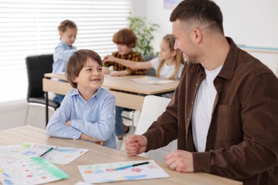Photo of Man teaching kid to draw at painting lesson indoors, selective focus