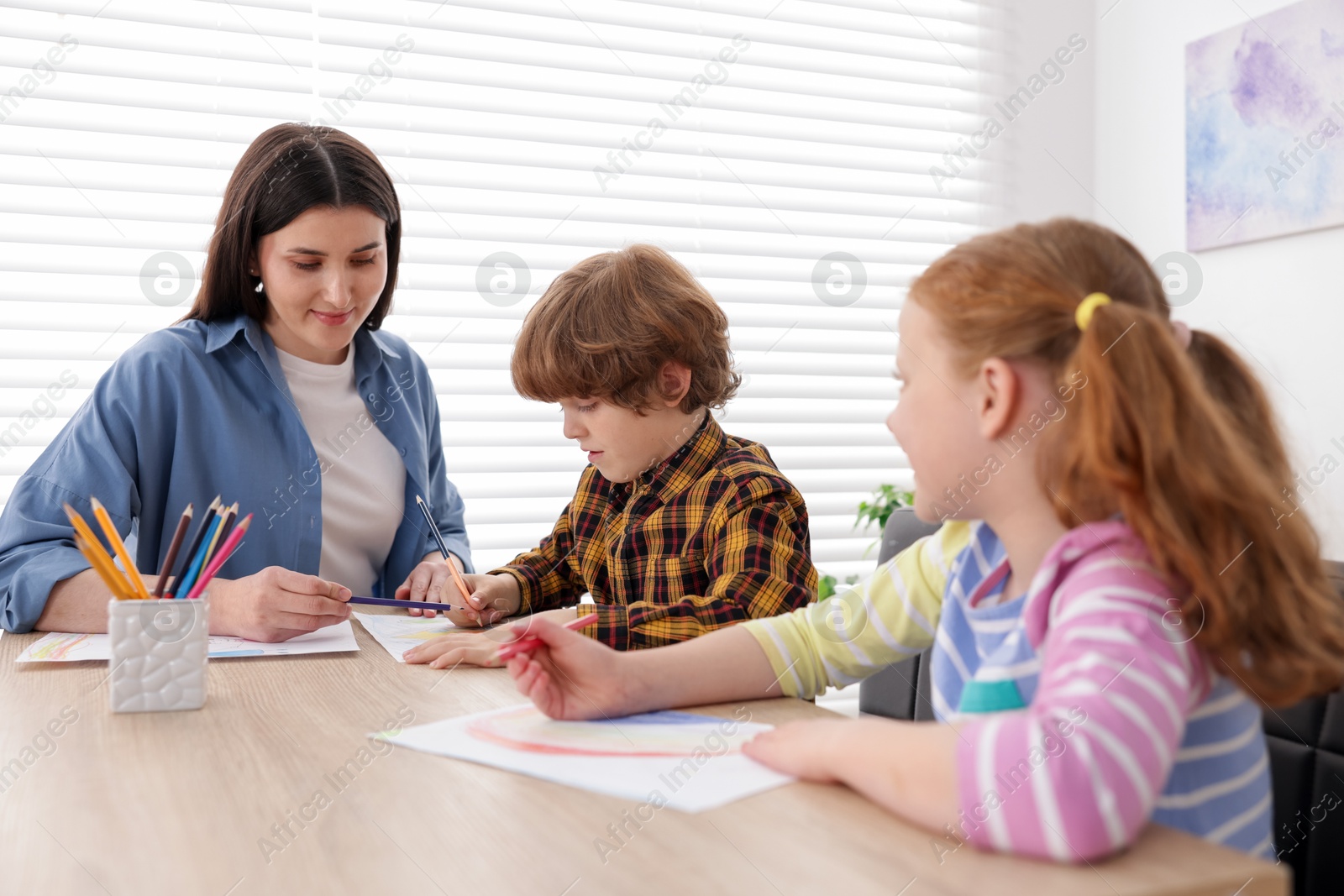 Woman teaching kids to draw at painting lesson indoors Photo of Woman teaching kids to draw at painting lesson indoors