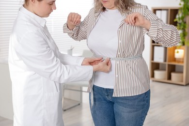 Photo of Weight loss. Nutritionist measuring overweight woman's waist with tape in clinic