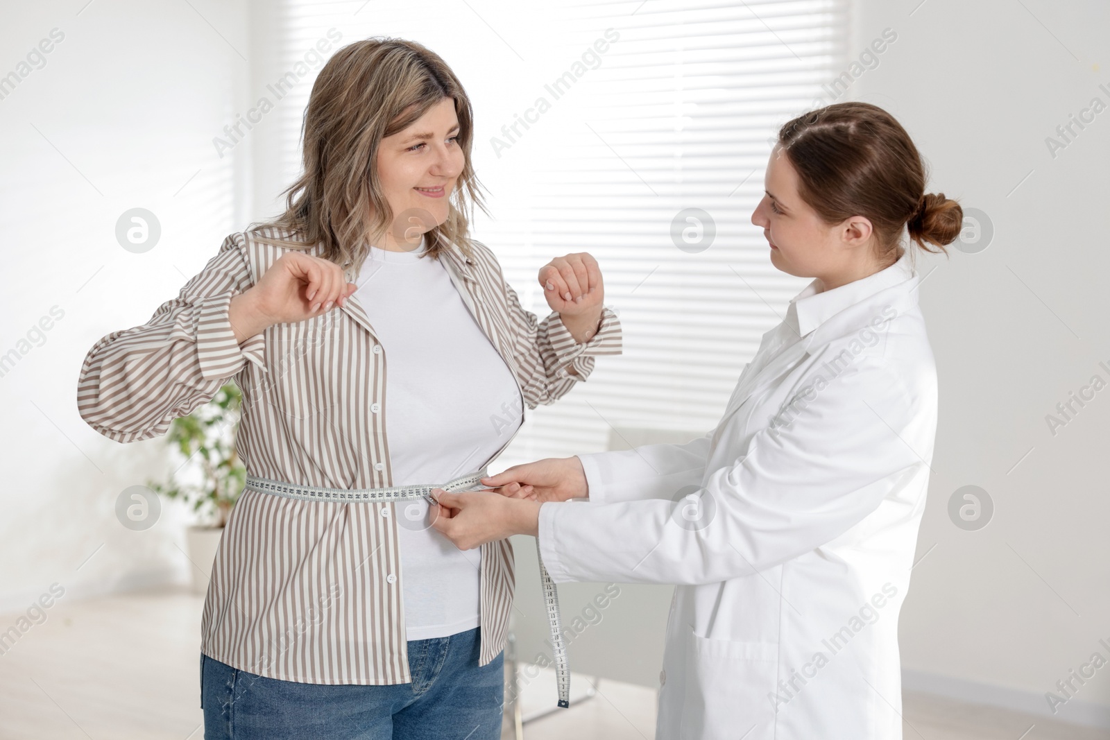 Weight loss. Nutritionist measuring happy overweight woman's waist with tape in clinic Photo of Weight loss. Nutritionist measuring happy overweight woman's waist with tape in clinic
