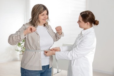 Photo of Weight loss. Nutritionist measuring happy overweight woman's waist with tape in clinic
