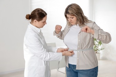 Photo of Weight loss. Nutritionist measuring overweight woman's waist with tape in clinic