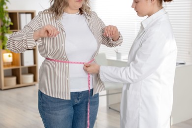 Photo of Weight loss. Nutritionist measuring overweight woman's waist with tape in clinic