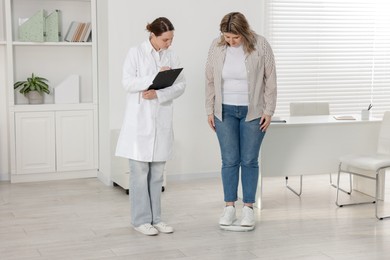 Photo of Weight loss. Overweight woman standing on scales during consultation with nutritionist in clinic