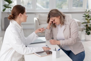 Photo of Weight loss. Nutritionist consulting upset overweight woman at white desk in clinic