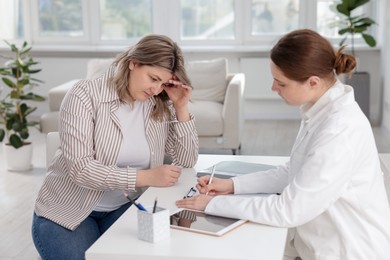 Photo of Weight loss. Nutritionist consulting upset overweight woman at white desk in clinic