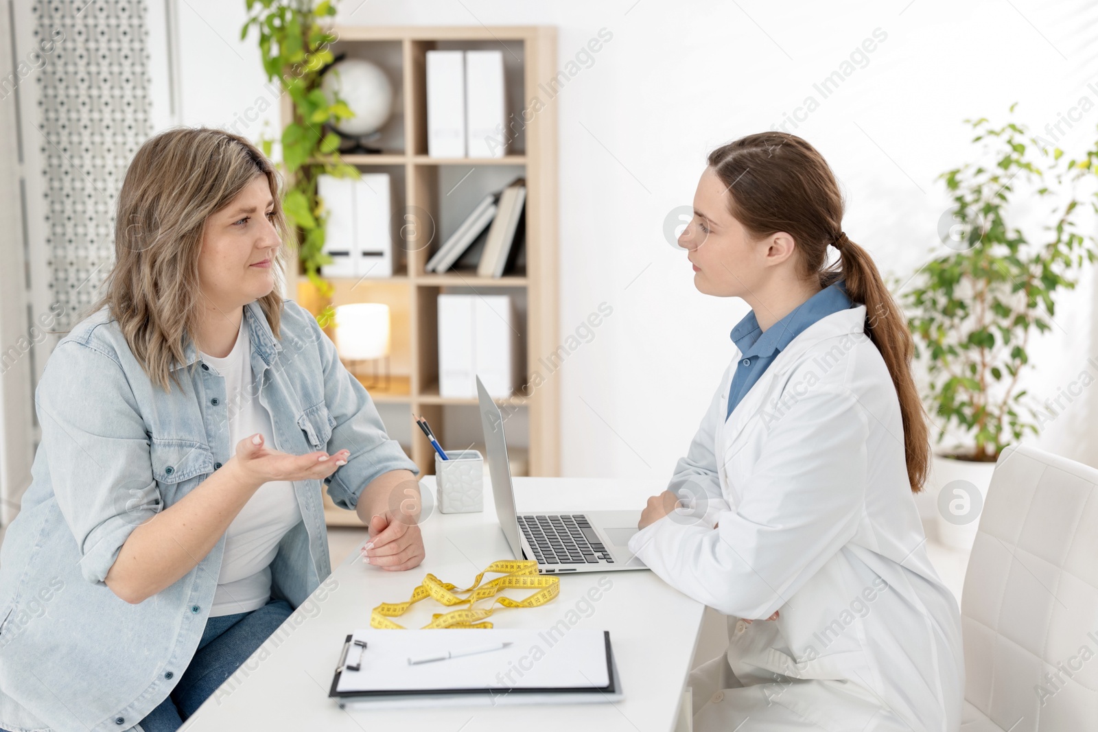 Weight loss. Nutritionist consulting overweight woman at white desk in clinic Photo of Weight loss. Nutritionist consulting overweight woman at white desk in clinic
