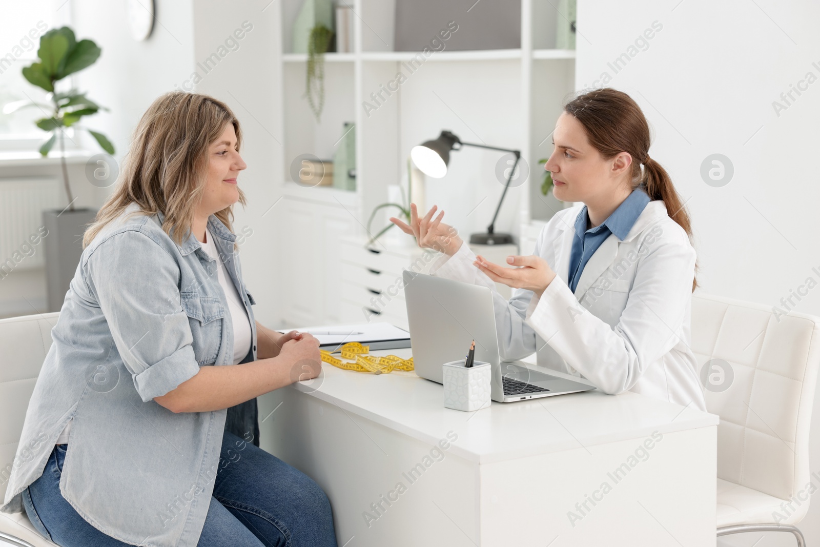 Weight loss. Nutritionist consulting overweight woman at white desk in clinic Photo of Weight loss. Nutritionist consulting overweight woman at white desk in clinic