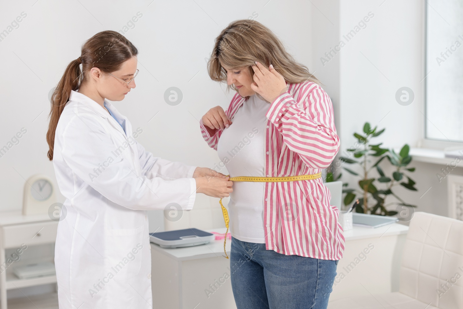 Weight loss. Nutritionist measuring overweight woman's waist with tape in clinic Photo of Weight loss. Nutritionist measuring overweight woman's waist with tape in clinic
