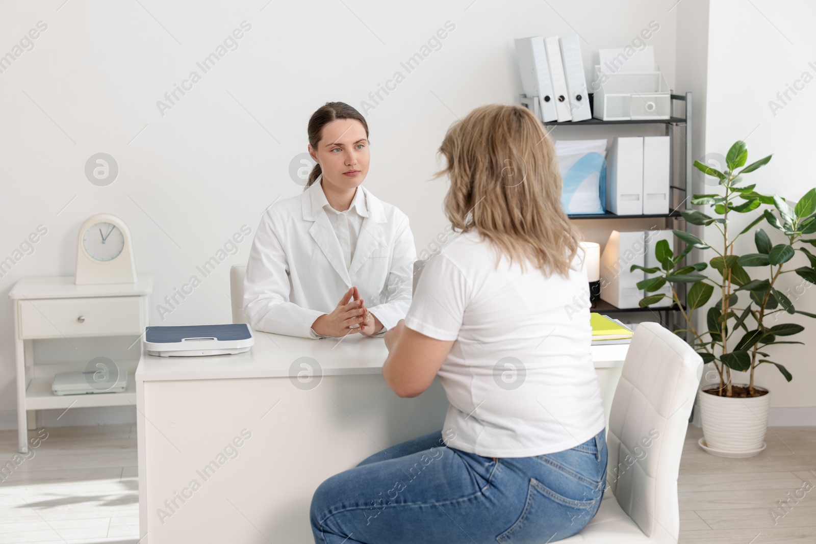 Weight loss. Nutritionist consulting overweight woman at white desk in clinic Photo of Weight loss. Nutritionist consulting overweight woman at white desk in clinic