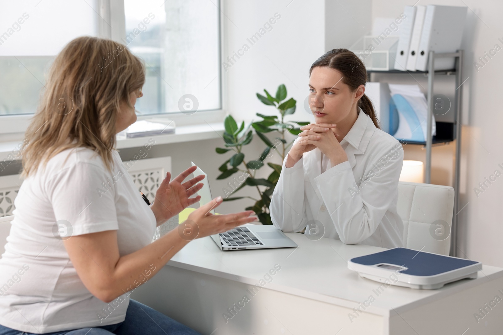 Weight loss. Nutritionist consulting overweight woman at white desk in clinic Photo of Weight loss. Nutritionist consulting overweight woman at white desk in clinic