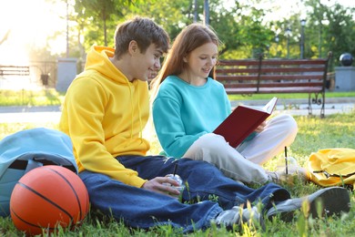 Photo of Teenage girl and boy reading together in park
