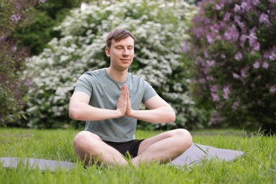 Photo of Young man practicing yoga on mat in park
