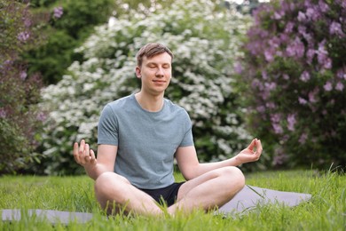 Photo of Young man practicing yoga on mat in park