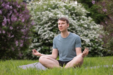 Photo of Young man practicing yoga on mat in park