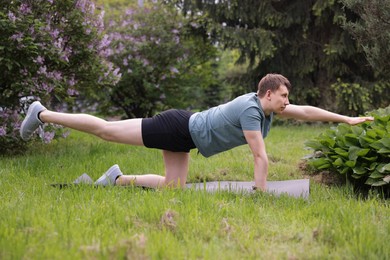 Photo of Young man practicing yoga on mat in park