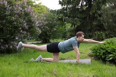 Photo of Young man practicing yoga on mat in park