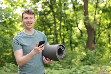 Photo of Young man with yoga mat and phone in park, space for text