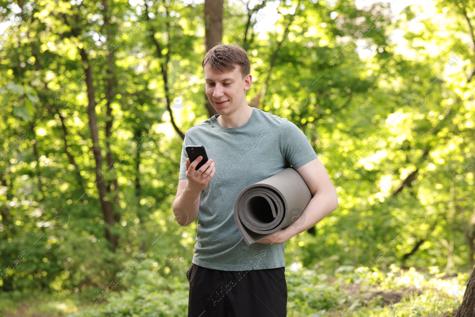 Young man with yoga mat and phone in park Photo of Young man with yoga mat and phone in park