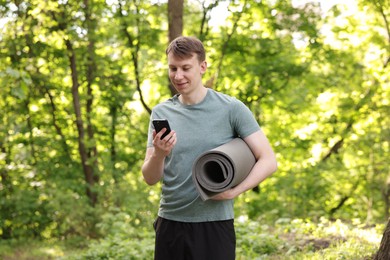 Photo of Young man with yoga mat and phone in park