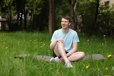 Photo of Young man practicing yoga on mat in park
