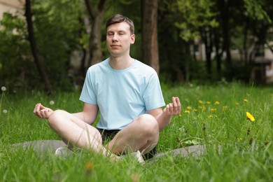 Photo of Young man practicing yoga on mat in park
