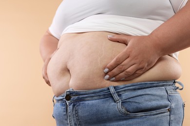 Photo of Woman with excessive belly fat on beige background, closeup