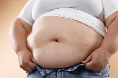 Photo of Woman with excessive belly fat on beige background, closeup