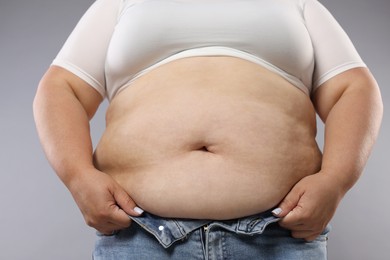 Photo of Woman with excessive belly fat on grey background, closeup. Overweight problem
